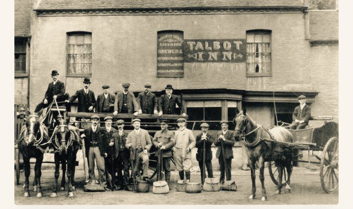 The Talbot Inn, with staff and customers gathered beneath the painted sign, horse-drawn delivery wagons in the street.