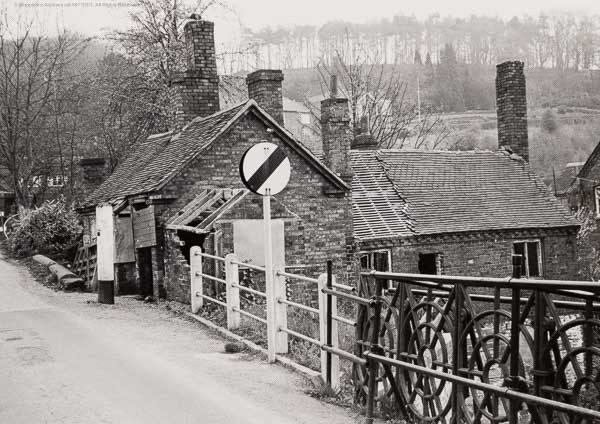 Toll house and neighbouring cottage stand together in this mid-twentieth-century view, no-entry and weight-limit signs crowding the approach between them. Visitors today still confuse the two buildings, so look carefully: one is the historic bridge toll house, the other a separate cottage that merely happens to share its doorstep with all this signage.