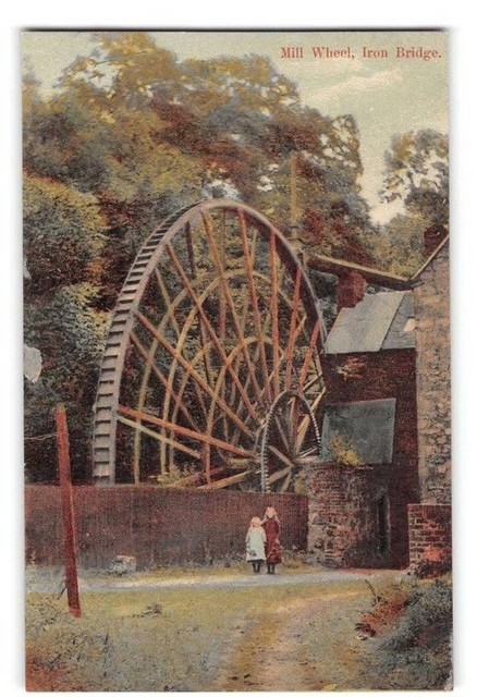 A coloured postcard titled "Mill Wheel, Iron Bridge", with two children standing in the lane below the wheel.