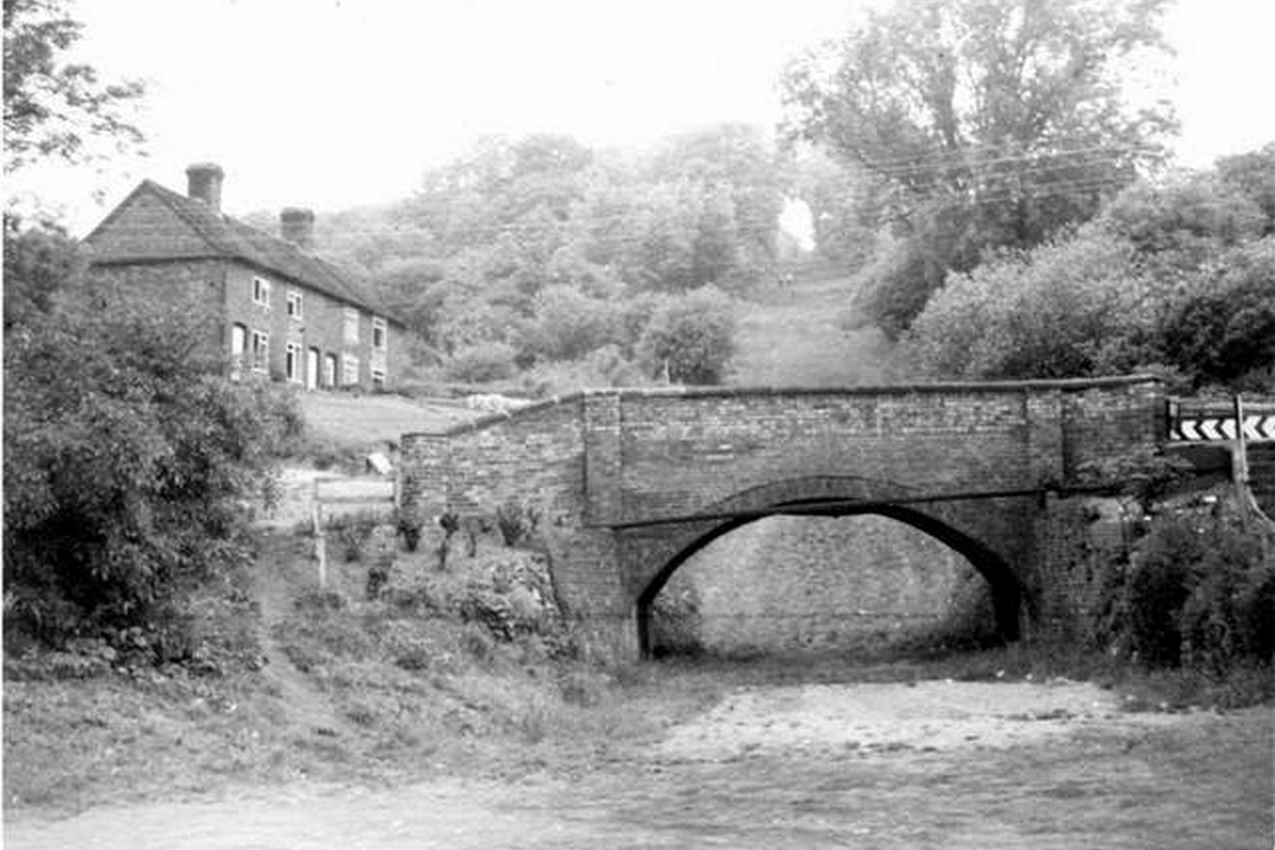 The brick bridge at the foot of the incline, with cottages beyond, photographed around the mid-twentieth century when this modest arch was almost all a passer-by would have noticed of the great machine rising above it. The incline itself lay hidden under decades of undergrowth, its history all but forgotten by casual visitors.