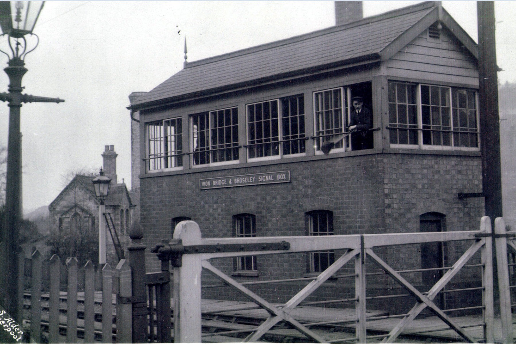 A signalman looks out from the window of the “Iron Bridge & Broseley” signal box in this photograph taken before 1956, the year the box closed for good. Its token instruments were then moved into the Station Master's office, a small but telling sign of the gradual simplification that preceded full closure.