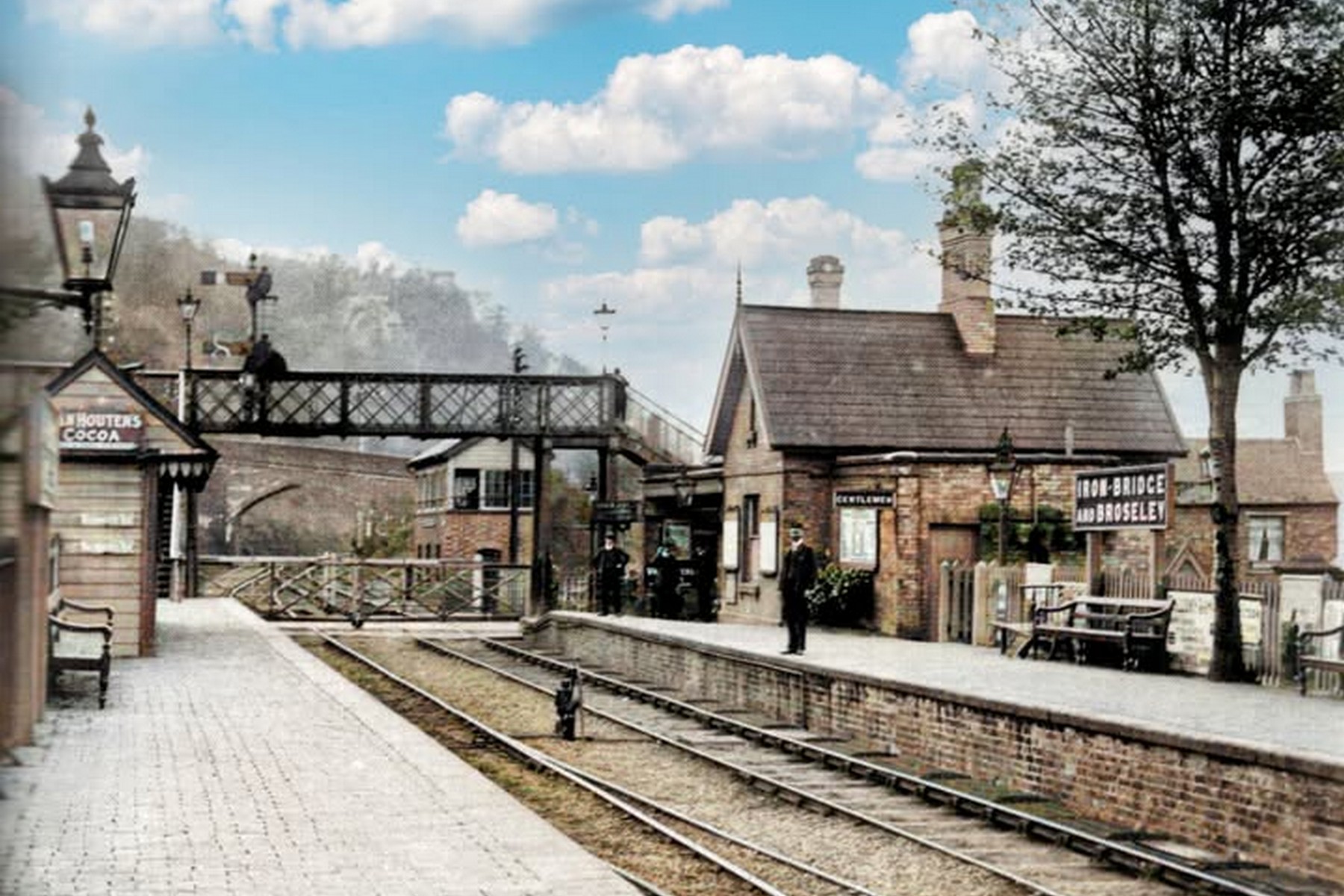 This undated, colourised photograph looks along the platform towards the footbridge and signal box, bringing footbridge, box and platform buildings together into a single frame. It's an unusually complete view of the station's working infrastructure, giving a good sense of how compact and self-contained the whole site actually was.