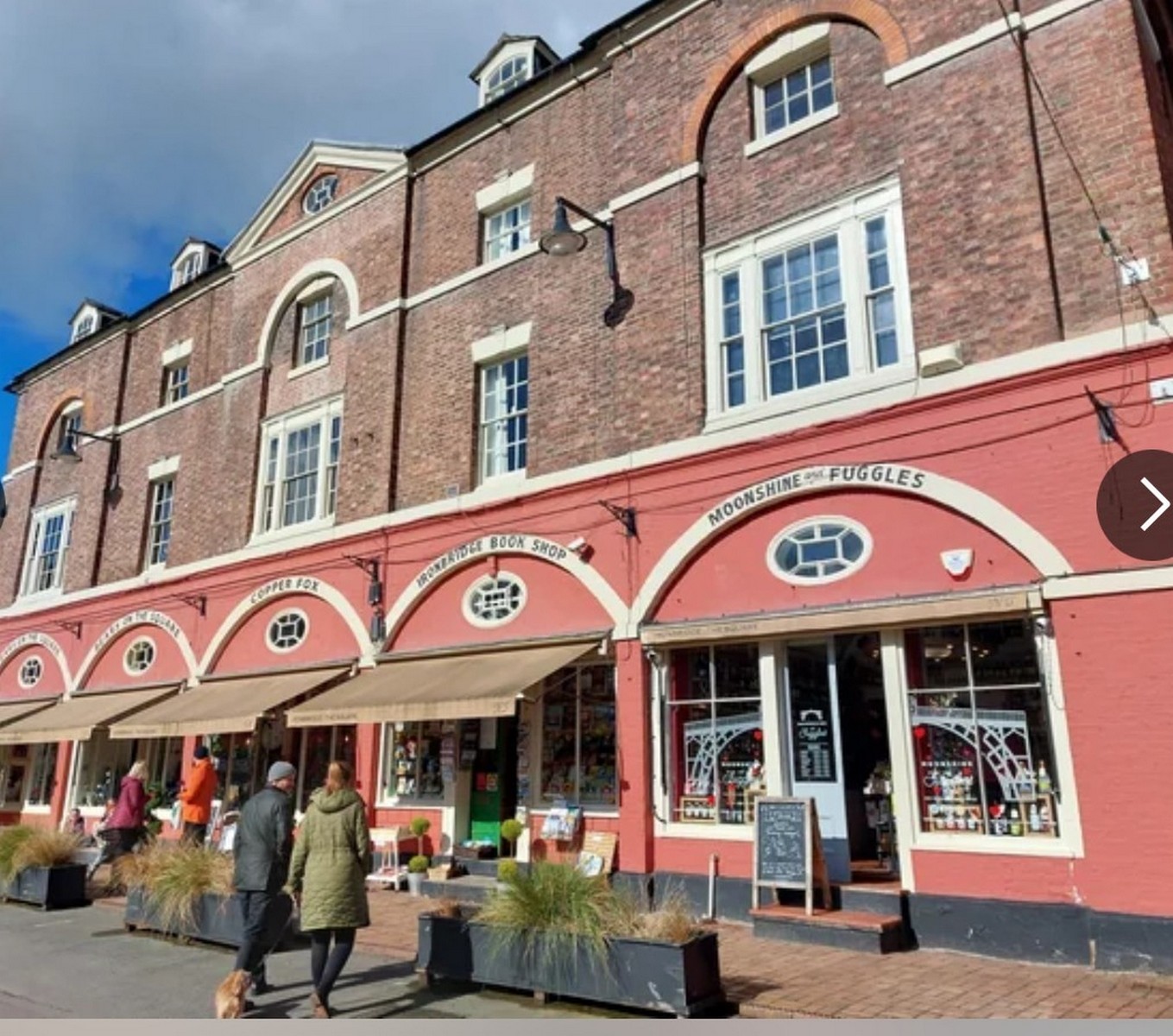 The arcade today in pink and cream, with The Book Nook, Ironbridge Book Shop and Moonshine & Fuggles trading under the arches. Different names, same openings: the building has simply kept finding new tenants for two centuries. Present day.