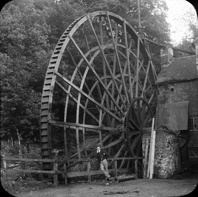 The giant waterwheel at Benthall Corn Mill, with a man standing at its foot for scale.
