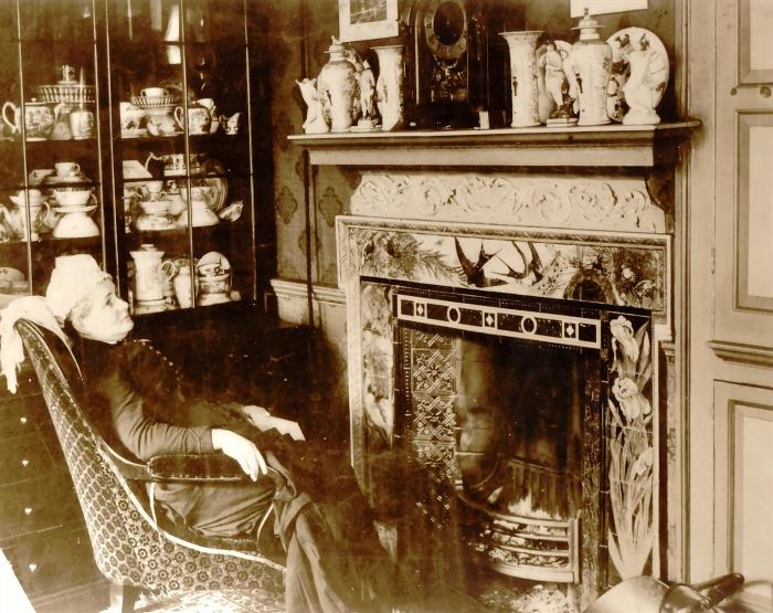 Grace Maw, seated in front of a tiled fireplace