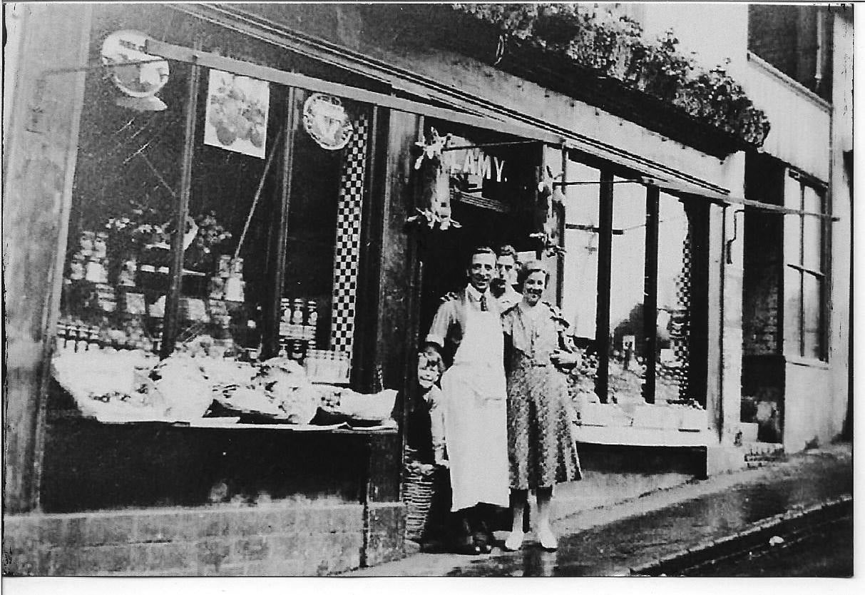 Shopkeepers and family outside their shop, its window display set out for the day