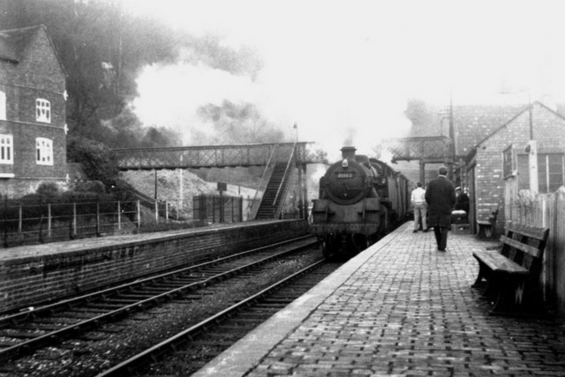A locomotive runs in as passengers wait patiently along the platform edge in this undated photograph from the steam era. Nothing dramatic is happening here, which is precisely the point — it's a snapshot of the everyday routine at a modest two-platform country station going about its ordinary business, likely sometime in the early 20th century.