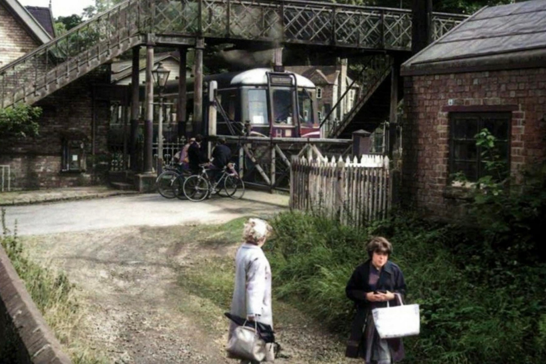 A diesel railcar waits at the crossing in this early 1960s photograph, cyclists and passengers gathered patiently by the gates. By this point steam had begun giving way to railcars on local services, a quiet technological shift that arrived only shortly before passenger trains stopped running here altogether in 1963.