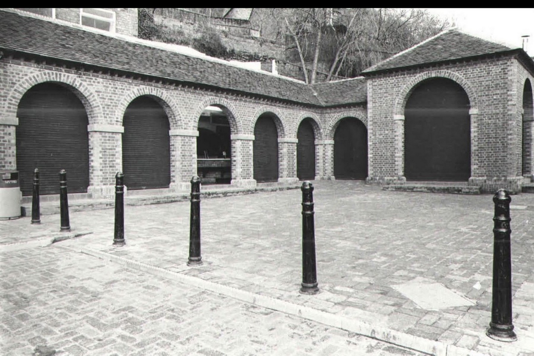The old market arcade seen from the courtyard, its brick arches now home to The Courtyard cafe. An open archway gives directly onto the paving, a modern use that still follows the old market rhythm: the space that once supplied traders now serves visitors. Late 20th century.