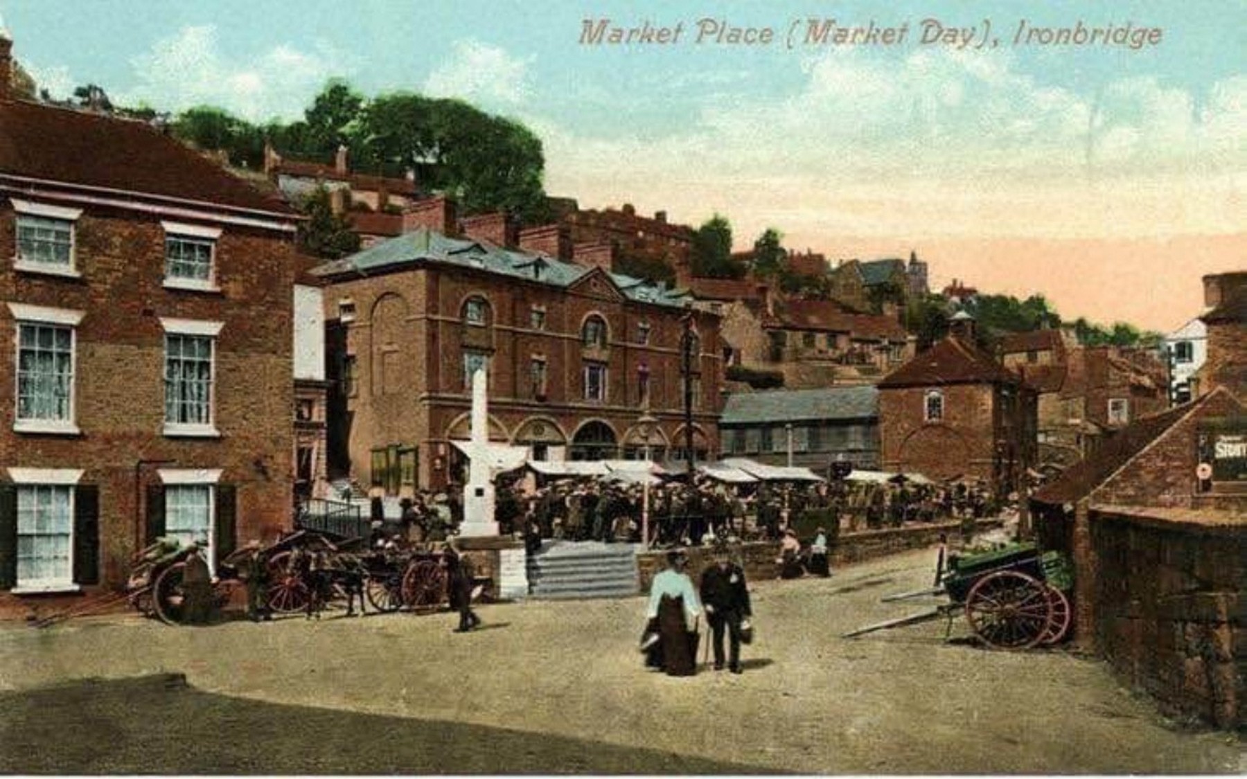 A printed commercial postcard, "Market Place (Market Day), Ironbridge" — proof that the market was considered a sight worth sending home. The tinting is hand-applied, so the colours are the printer's guesswork rather than the truth. Postcards like this carried the town's image across Britain. Exact date unknown.