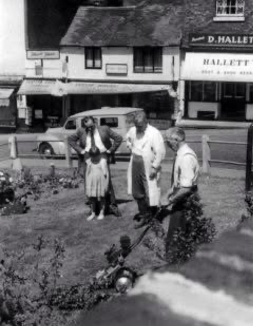 Tending the beds in the Square, with D. Hallett's boot and shoe repairs behind