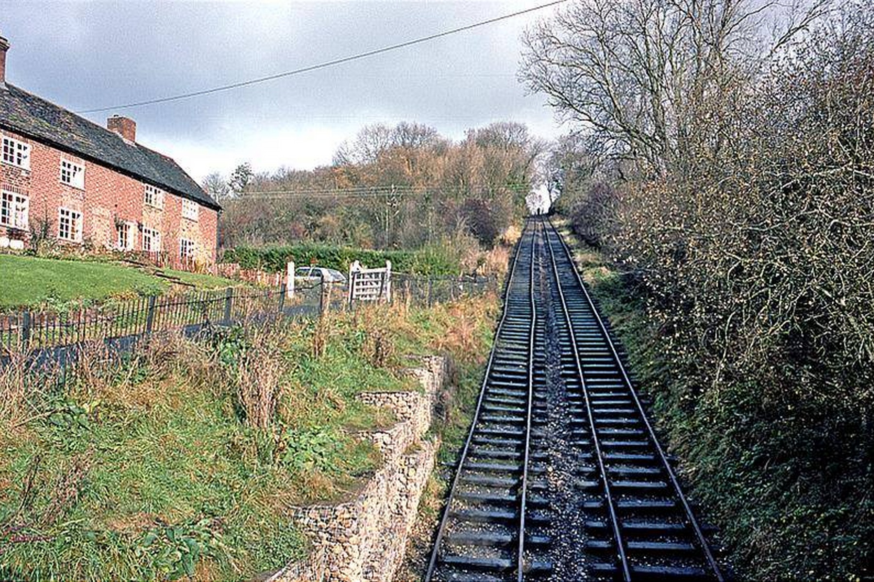 Rails run uphill past a brick cottage and stone gabion walls in this present-day view — a detail worth noticing is just how close the houses sit to the track. People still live within a few feet of one of Britain's great industrial monuments, a reminder that this was always a working, lived-in landscape rather than a museum piece.