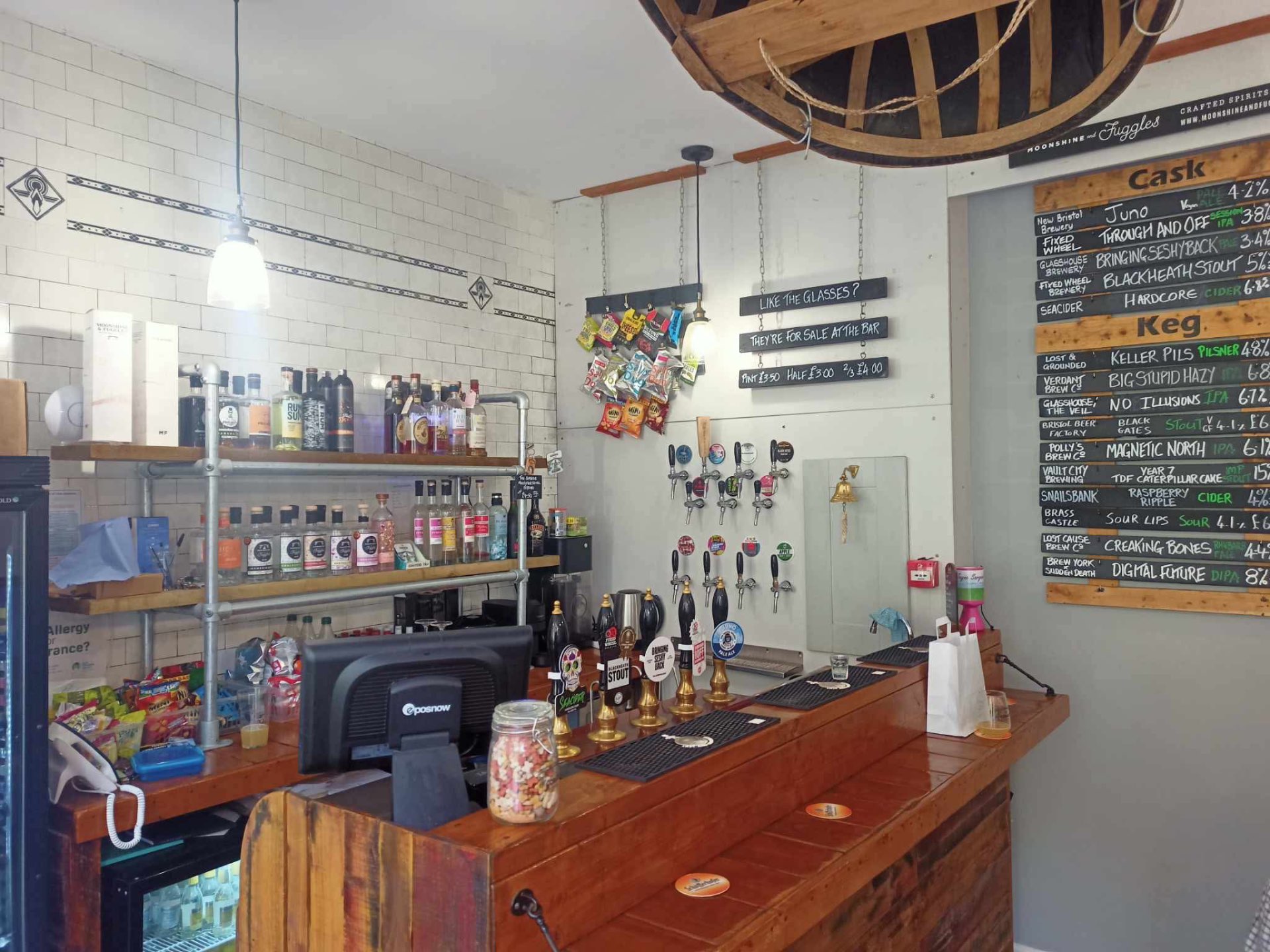Inside The Coracle Micropub: the bar, cask and keg taps, with a small barrel wheel on the ceiling.