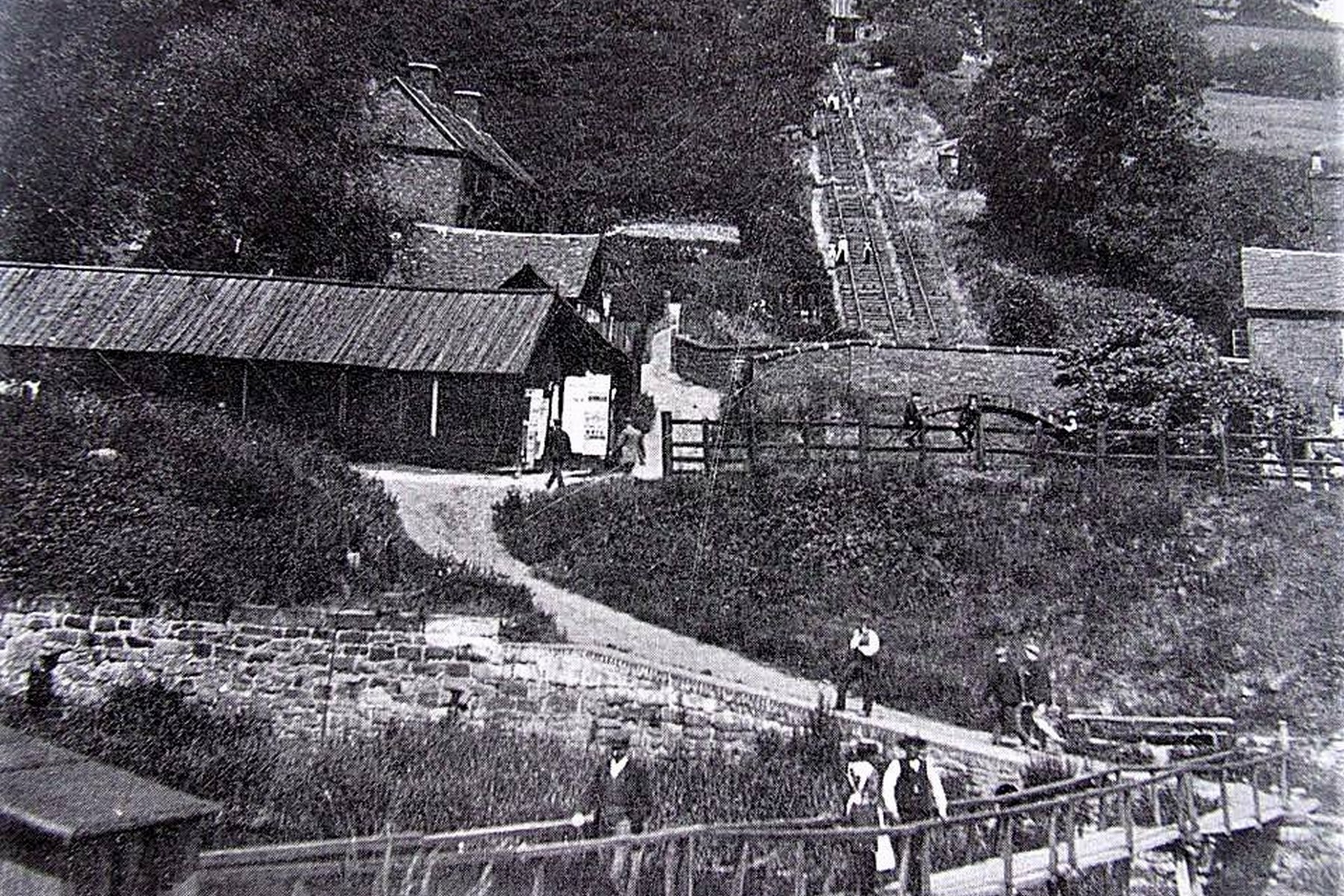 Looking up from the Coalport valley floor towards the incline, with works and cottages crowded in the foreground, this early-1900s view captures the everyday traffic of the place: coal, iron, clay and finished Coalport china all travelled this route between Blists Hill and the Severn wharves. It's easy to forget, standing here today, how industrial this quiet corner once felt.