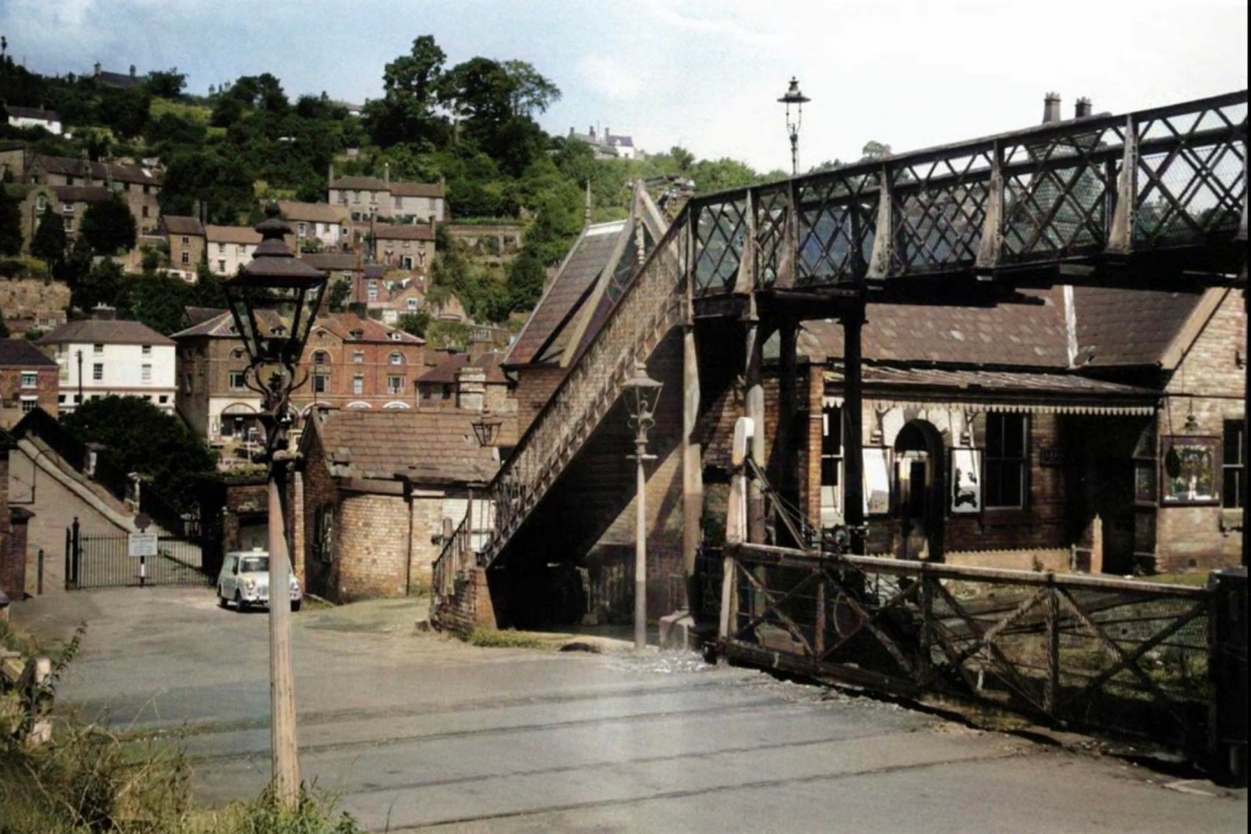 Photographed in the 1960s, this view of the footbridge and station approach shows Ironbridge climbing the hillside directly behind. The steepness of that slope explains a great deal about the station's cramped layout — there was simply nowhere else to put it, squeezed as it was beneath the town it served.